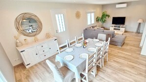 Una sala de estar moderna con comedor, un conjunto de sofás, un televisor y una planta.