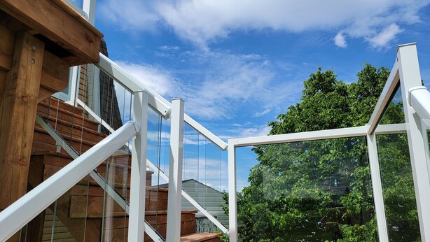 Una terraza de madera con barandas de vidrio y una vista despejada del cielo y los árboles.
