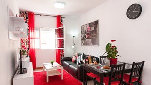 Ein modernes Wohnzimmer mit einem schwarzen Ledersofa, einem Esstisch mit Stühlen, einem roten Teppich und einer Zimmerpflanze.