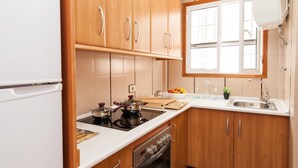 Eine Küche mit Holdelementen, einer weißen Arbeitsplatte, einem Herd, einem Backofen, einer Spüle und einem Fenster mit Jalousien.