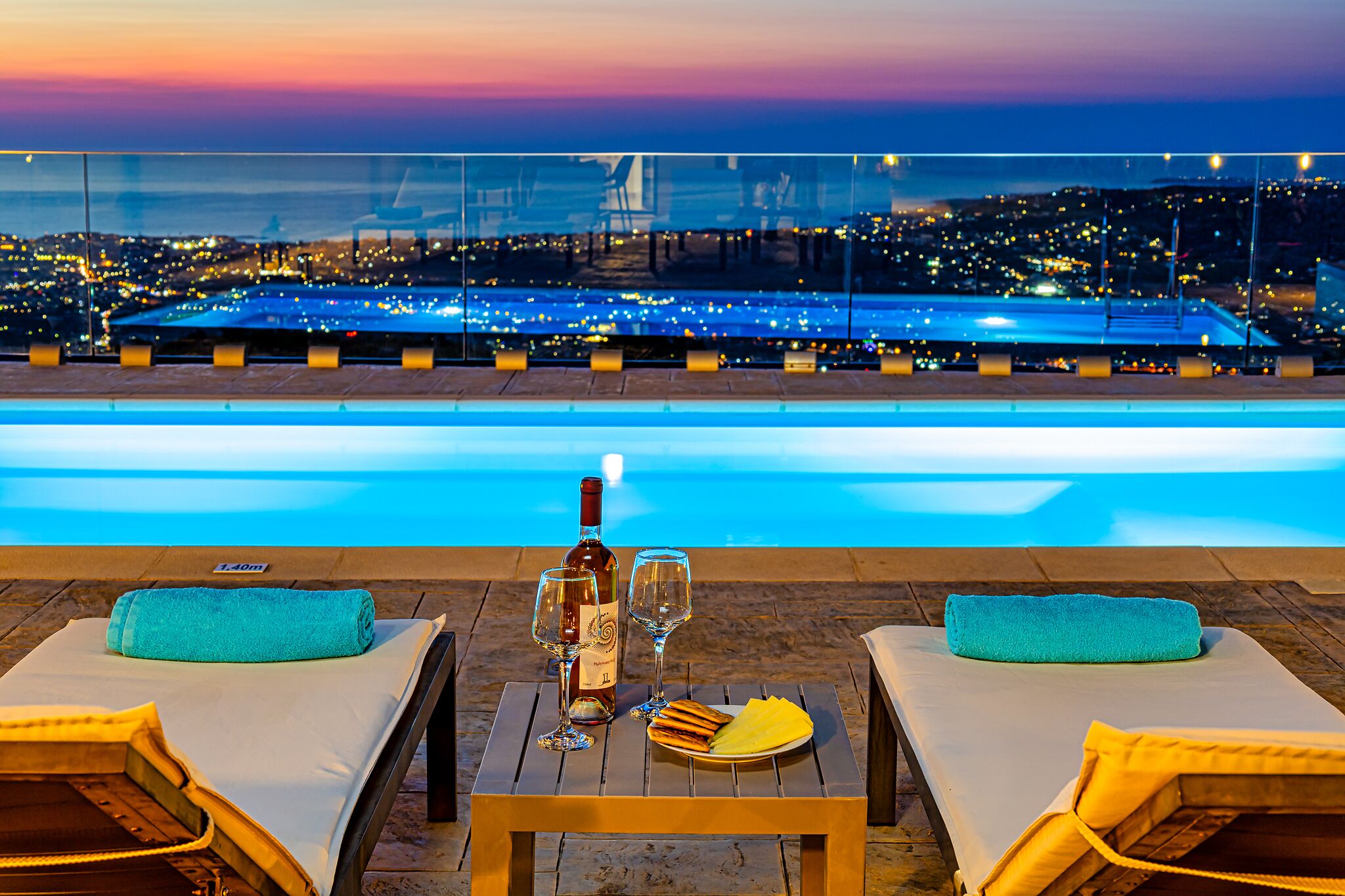 A poolside setting with a sunset view, a bottle of wine, and a plate of food on a table.