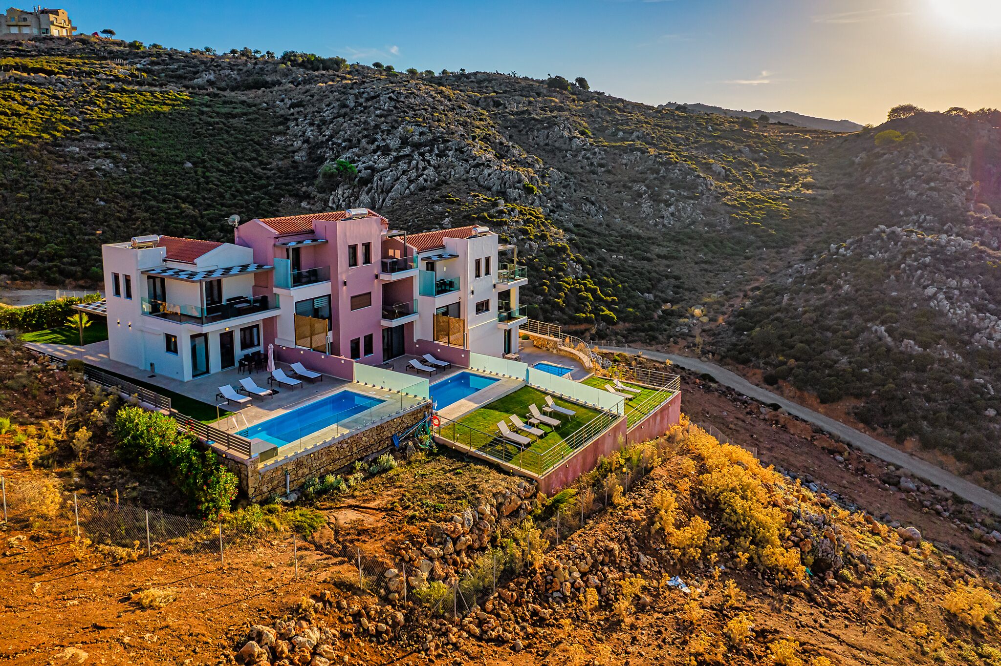 A multi-story villa with a swimming pool, located on a hillside with a view of the surrounding landscape.