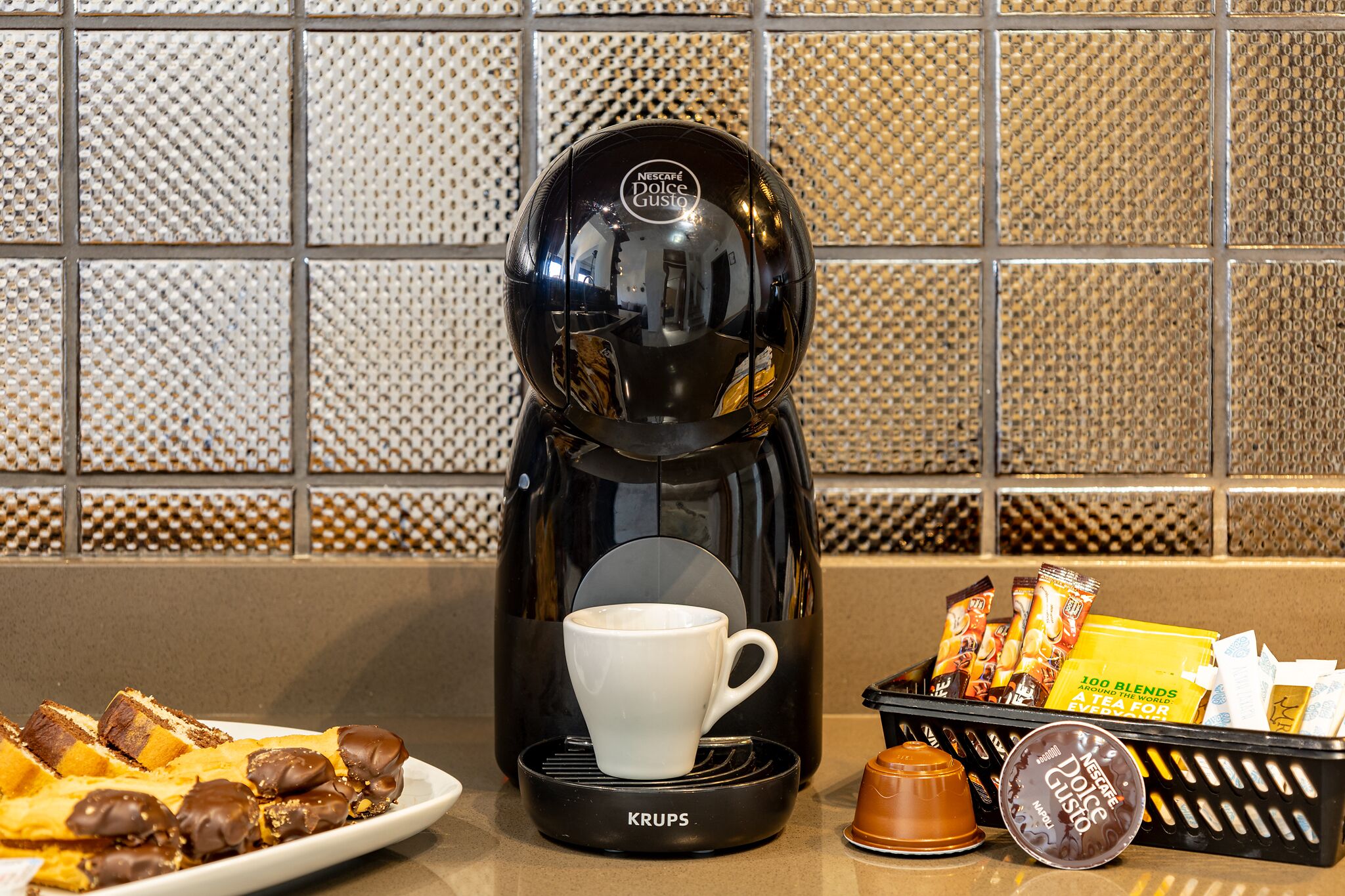A coffee maker with a cup, waffles, and a basket of snacks.