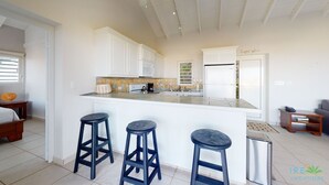 A modern kitchen with white cabinets, a large island with stools, and a view of the outdoors. - ☀️🌴Breezy Bird by IRE Vacations - Cozy 2 bedroom Villa with Private Pool (Oyster Pond)