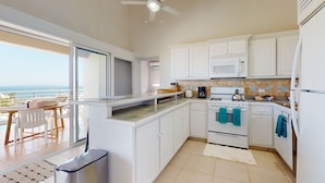 A modern kitchen with white cabinets, a stove, and a microwave. There is a dining area with a table and chairs visible through a glass door. - ☀️🌴Breezy Bird by IRE Vacations - Cozy 2 bedroom Villa with Private Pool (Oyster Pond)