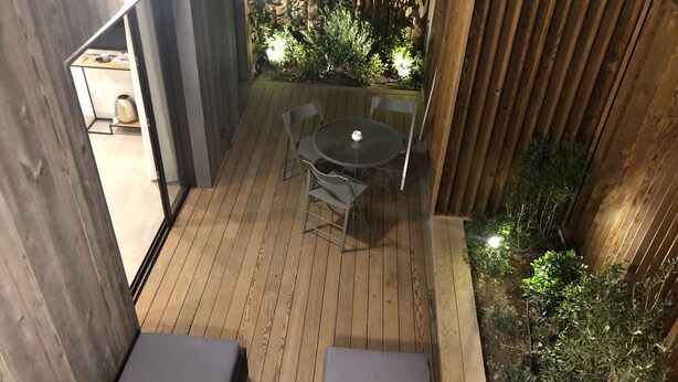 En träaltan med ett bord och stolar, omgiven av växter och ett trästaket.