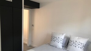 Ett sovrum med en säng, två kuddar med cirkelformade mönster, ett vitt sängöverkast och en mörkfärgad garderob.