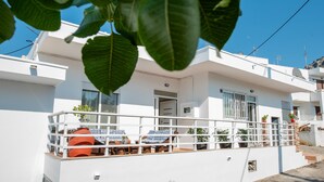 Una casa moderna de color blanco con un balcón, un pequeño jardín y un cielo azul despejado.