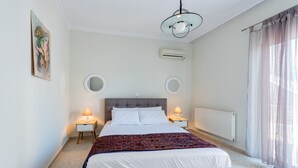 Un dormitorio con una cama grande, dos mesitas de noche con lámparas, un candelabro en el techo, un equipo de aire acondicionado, un radiador y una ventana con cortinas.