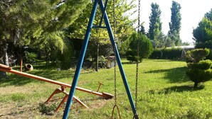 A swing set in a grassy outdoor area with trees and a clear sky. - Urla Bella  (Urla)