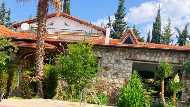 A poolside dining area with a stone building, a pool, and lush greenery. - Urla Bella  (Urla)