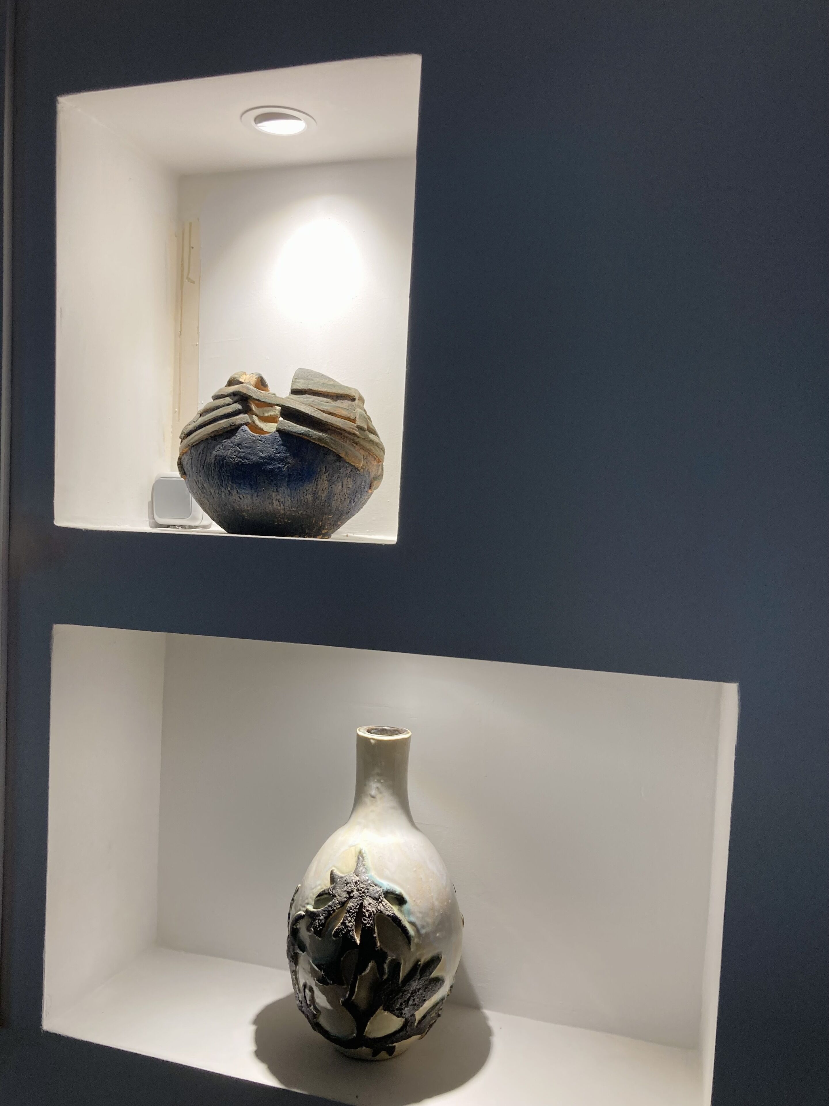 Two ceramic vases displayed in white shelves against a dark wall.