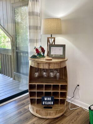 A wooden wine rack with glasses, a lamp, and a framed certificate on a table by a window.