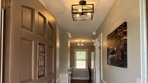 A hallway with a wooden floor, a modern light fixture, a refrigerator, and a door with a security lock. - West Asheville~Biltmore Estate~River Arts District~pet friendly (Asheville)