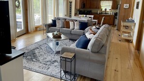A spacious living room with a grey sofa, a coffee table, and a TV. There is a kitchen in the background with wooden cabinets and a dining area. - Snowmobile & ATV right on our property to trails, Ride the wilds, corridor 5. (Stark)
