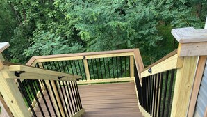 A wooden deck with a metal railing, surrounded by dense green foliage. - Hot Tub Mountain View Dog Friendly Modern Chalet (Linden)
