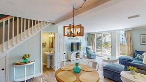 Un salón amplio con una escalera, una mesa de comedor con individuales, un sofá y un televisor.