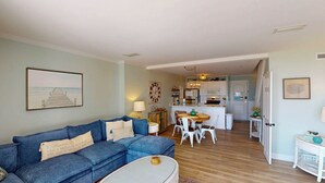 Una sala de estar con un sofá azul, una zona de comedor con una mesa redonda y una cocina al fondo.