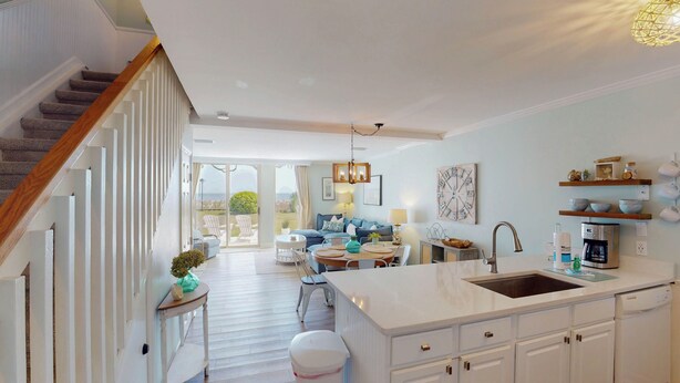Una cocina moderna con una isla grande, un comedor con mesa y sillas, y una sala de estar con sofá y vistas a través de puertas de vidrio.