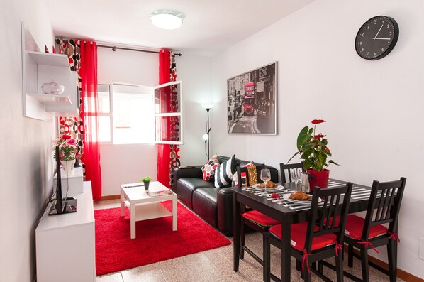 A modern living room with a black leather sofa, a dining table with chairs, a red rug, and a potted plant. - Kasa apartment, one step away from Las Canteras beach. (Las Palmas de Gran Canaria)