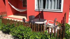 Un edificio rojo con una hamaca, una mesa con sillas y una ventana con cortinas.