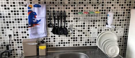A kitchen with a stainless steel sink, a tiled backsplash, and various kitchen utensils hanging on the wall.