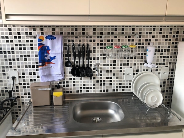 A kitchen with a stainless steel sink, a tiled backsplash, and various kitchen utensils hanging on the wall.