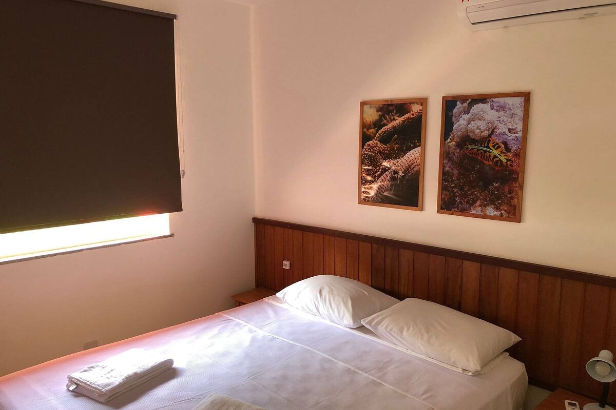 A neatly made bed with white linens, a wooden headboard, and two framed pictures on the wall.