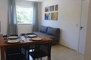 Un comedor con una mesa dispuesta para cuatro, un sofá gris y una ventana con cortinas.