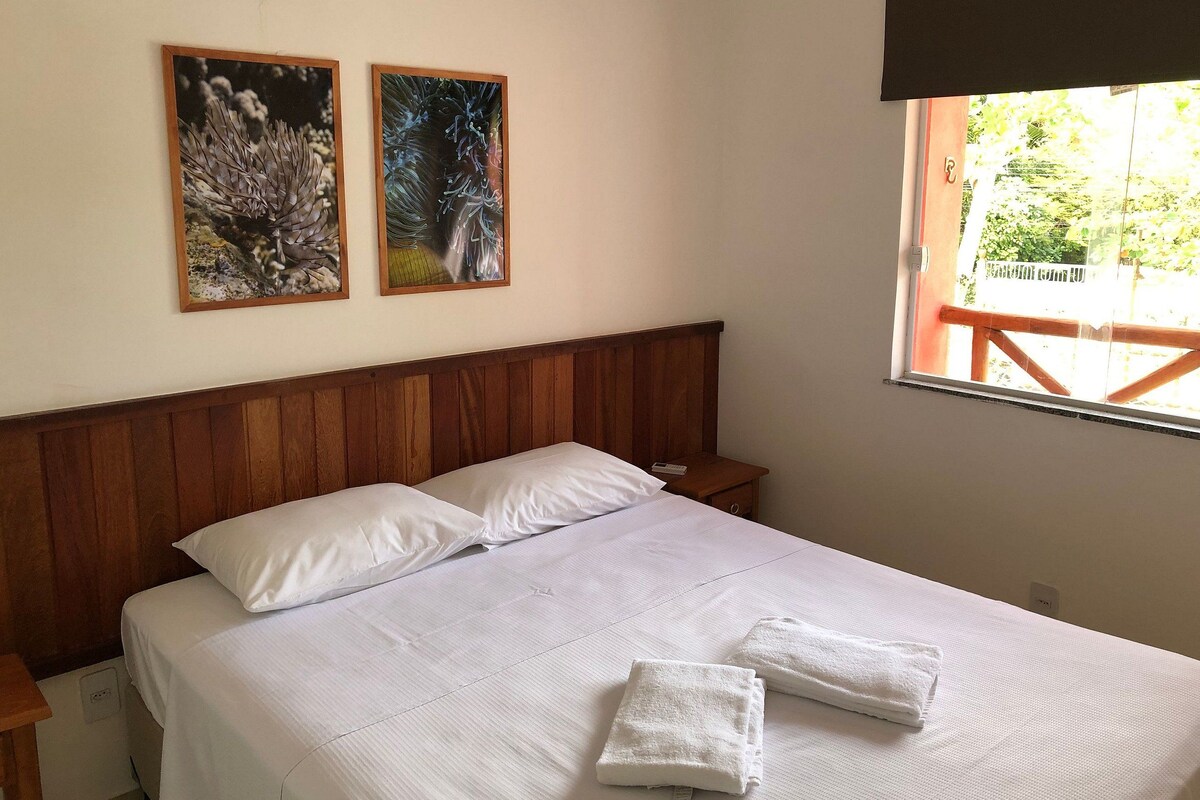 Una cama bien hecha con sábanas blancas y dos almohadas, cabecera de madera y dos obras de arte enmarcadas en la pared.
