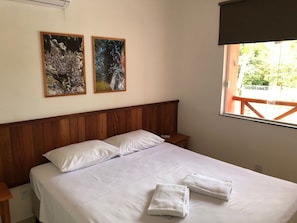 Una cama bien hecha con sábanas blancas y dos almohadas, cabecera de madera y dos obras de arte enmarcadas en la pared.