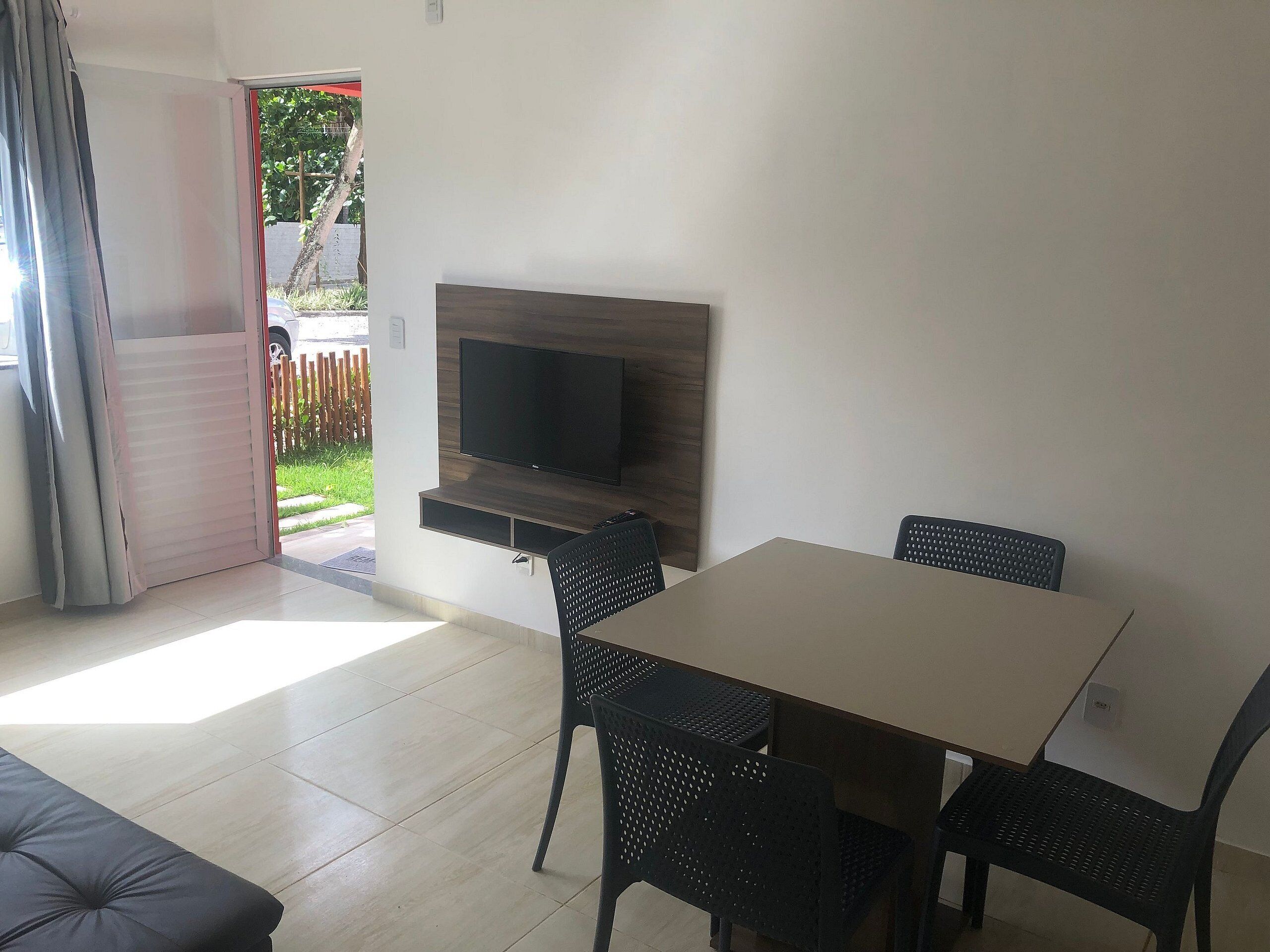 Een moderne woonkamer met een flatscreen televisie bevestigd aan een houten wand, een eettafel met vier stoelen, en een schuifdeur naar een buitenruimte.