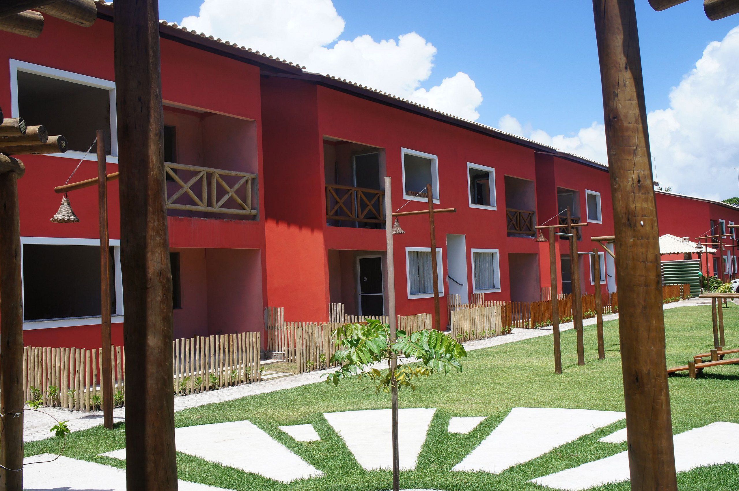 Un edificio rojo con múltiples ventanas y balcones, rodeado por una cerca de madera y un pequeño césped.
