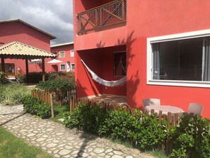 A red building with a hammock, a wooden fence, and a paved pathway. - Apartamento na região de Guarajuba (Camaçari)