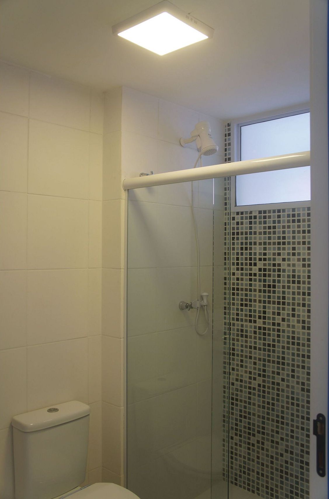 Un baño con cabina de ducha de vidrio, inodoro y ventana.