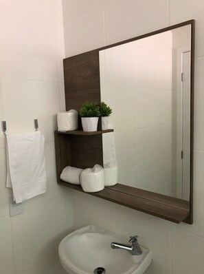 A bathroom with a white sink, a mirror, and a towel rack. - Apartamento na região de Guarajuba (Camaçari)