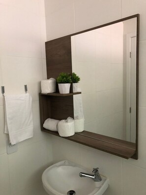 Un baño con lavamanos blanco, un espejo y un perchero para toallas.