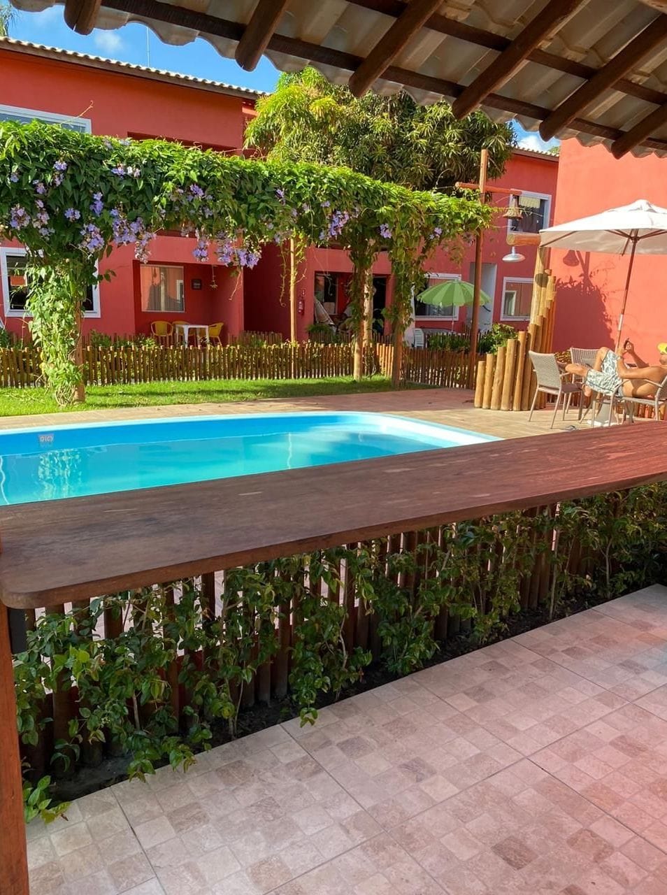 A swimming pool with a wooden deck, surrounded by a bamboo fence and potted plants.