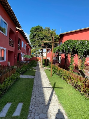 Un camino que lleva a un edificio de fachada roja, rodeado de césped cuidado y una valla de madera.
