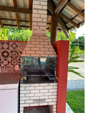 Un horno de ladrillo al aire libre con una parrilla de metal, rodeado por un muro con diseños y un pilar rojo.