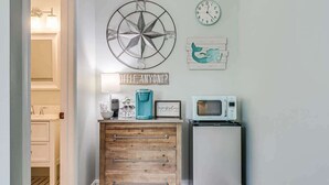 A kitchen with a wooden cabinet, a coffee maker, a microwave, and a wall clock.