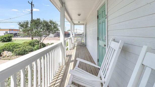 A porch with white railings and a green door, leading to a building with a white exterior.