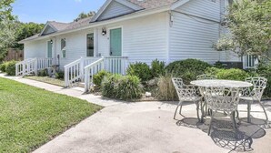 Uma casa de dois andares com varanda da frente, um pequeno jardim e um alpendre com mesa e cadeiras.