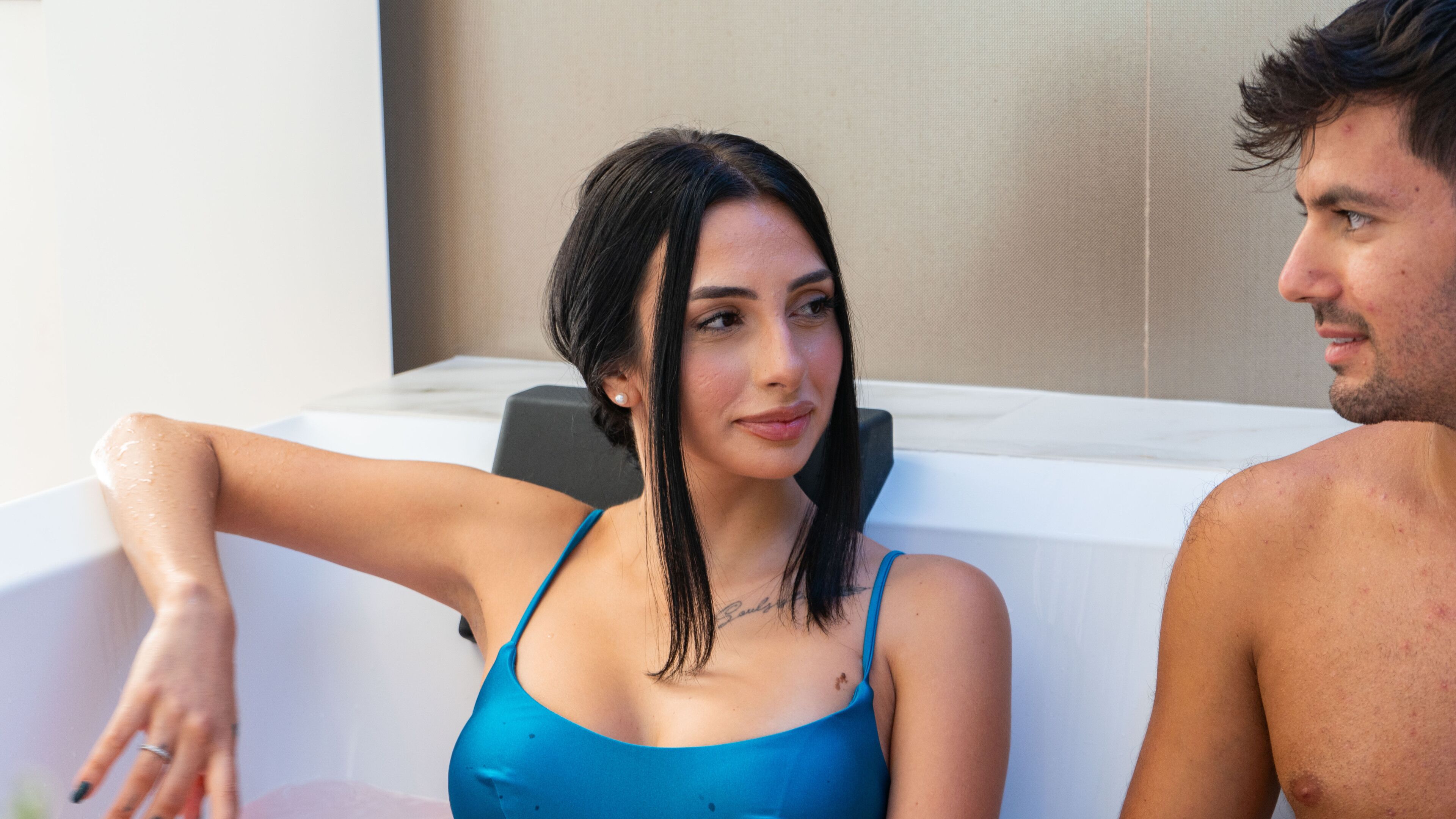 Une femme en maillot de bain bleu est assise dans une baignoire, un homme étant assis à ses côtés.