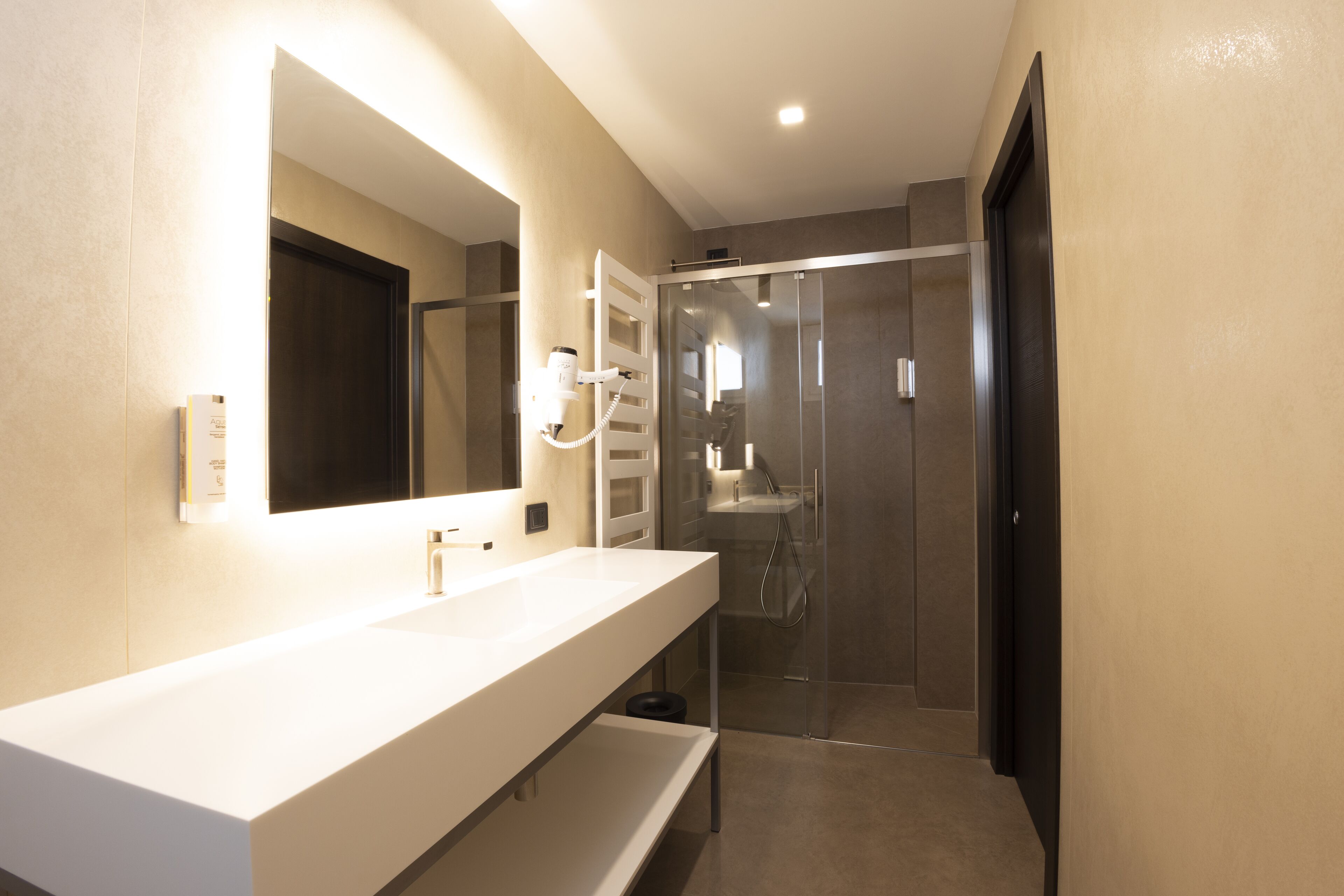 Un baño moderno con un espejo grande, un tocador blanco y una ducha con mampara de vidrio.
