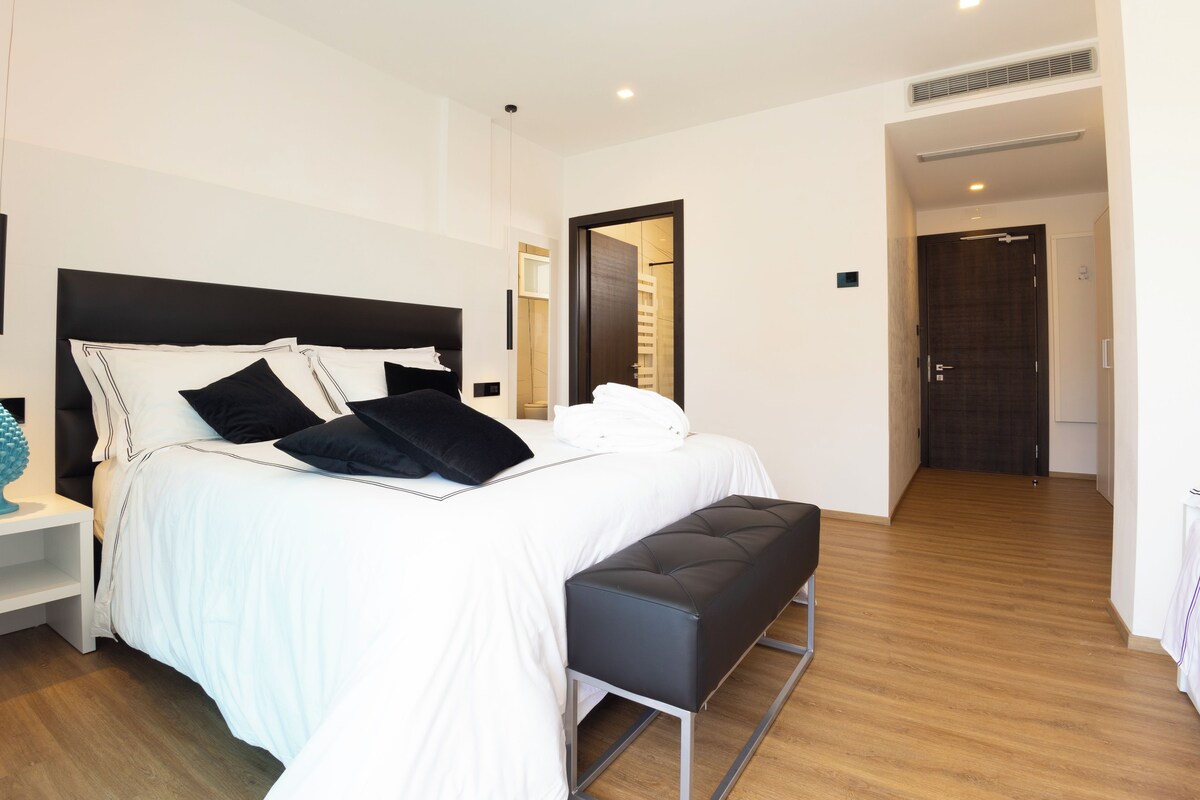 Un dormitorio moderno con una cama grande, un banco, una mesita de noche y un espejo.