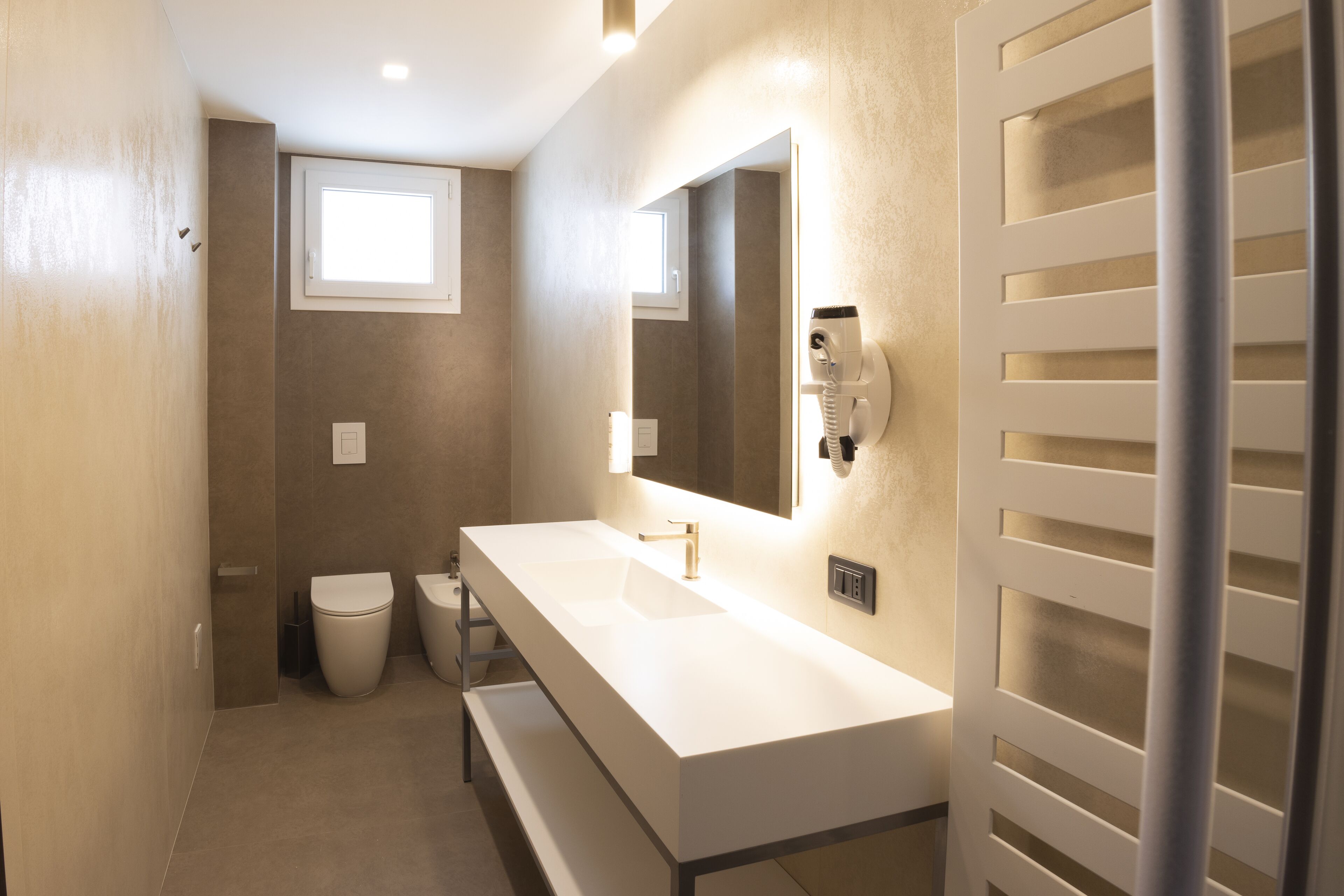 A modern bathroom with a white sink, a mirror, and a hairdryer mounted on the wall.
