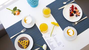 Un desayuno con un menú, un jarrón decorativo azul, una bebida amarilla y un plato de fruta y postre.
