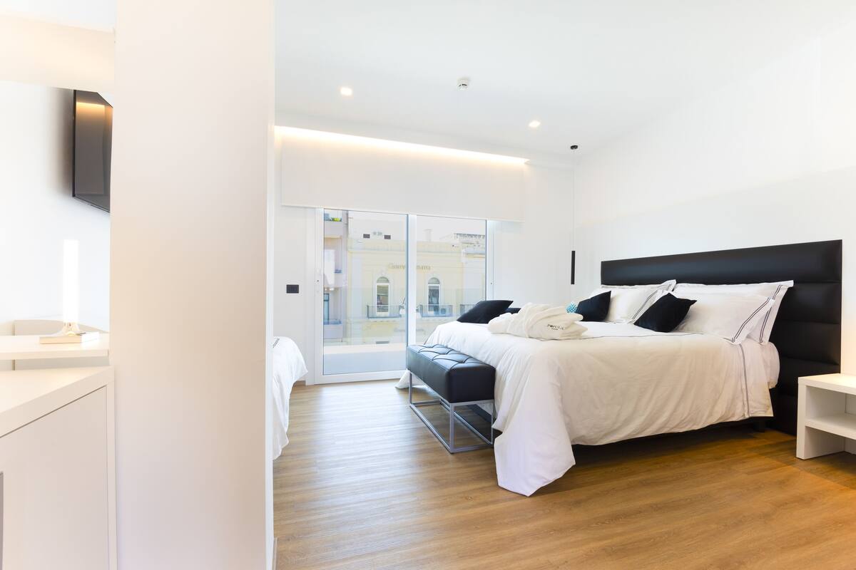 A modern bedroom with a large bed, a bedside table, and a view through a glass door.