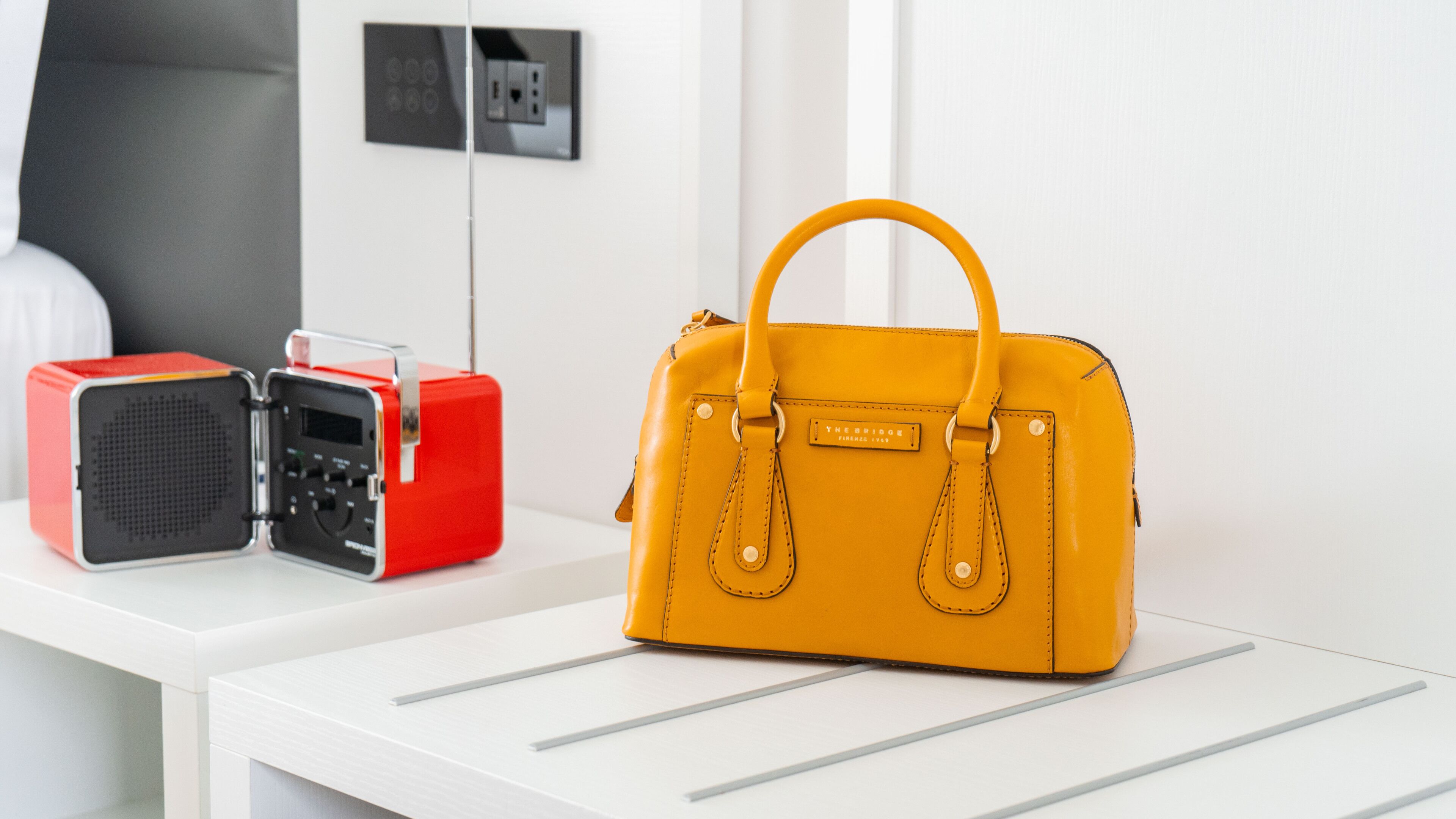 A yellow handbag on a white table with a red and black radio beside it.